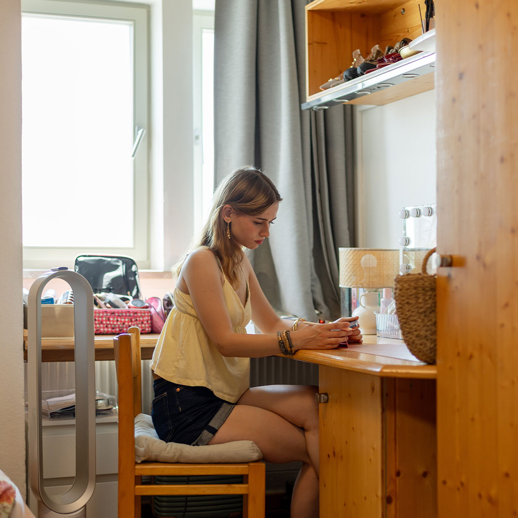 Junge Frau blickt konzentriert aufs Handy am hellen Holztisch, gelb und grau