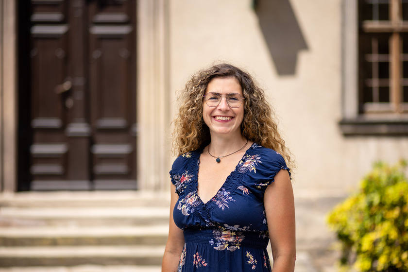 Laechelnde Frau mit Locken und Brille in blauem Blumen Kleid im Freien
