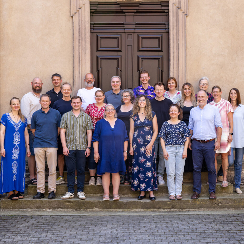 Laechelnde Gruppe in bunten Outfits vor grosser brauner Holztuer