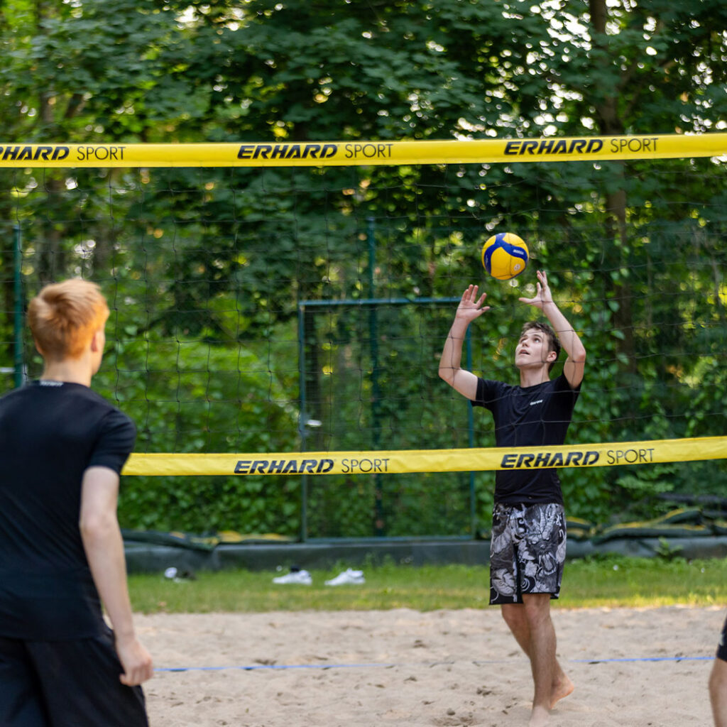 Fokussierter junger Mann in Schwarz spielt Beachvolleyball am Netz in Gelb