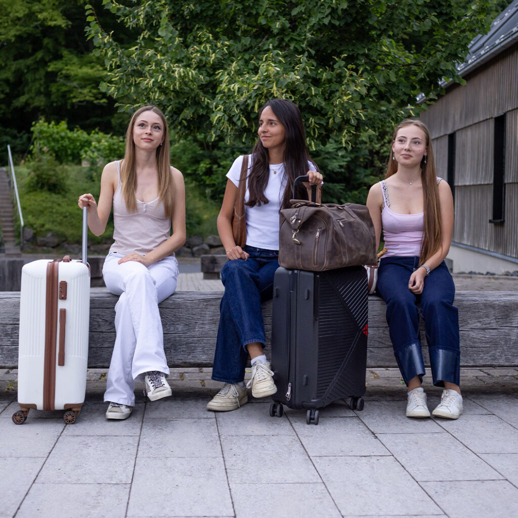 Drei Frauen schauen entspannt, mit hellen und dunklen Koffern und Tasche