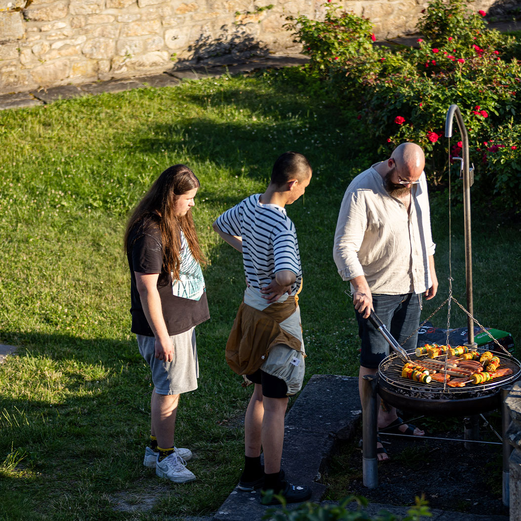 Drei Personen schauen ernst auf bunten Grill im gruener Garten