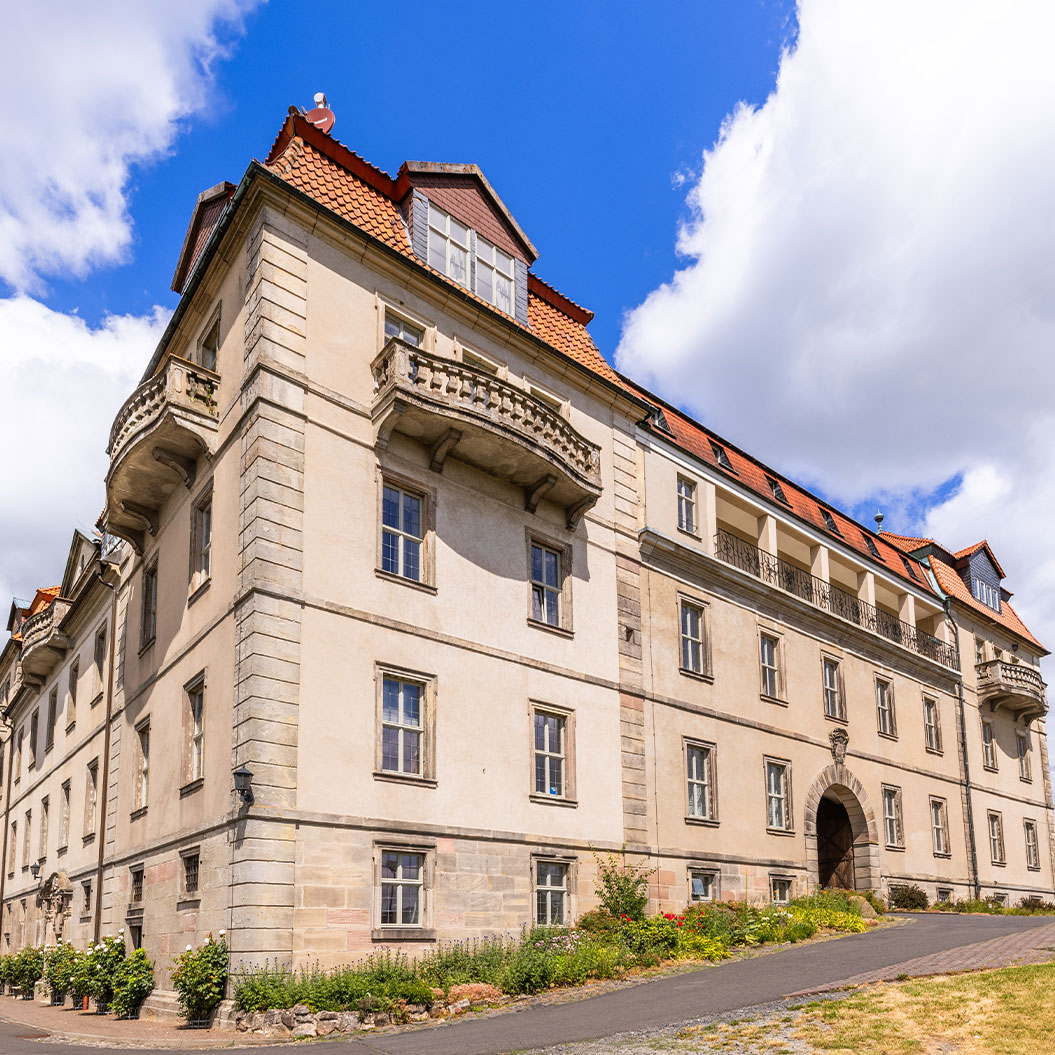 Beiges Altbaugebaeude mit rotem Dach und Balkonen unter blauem Himmel