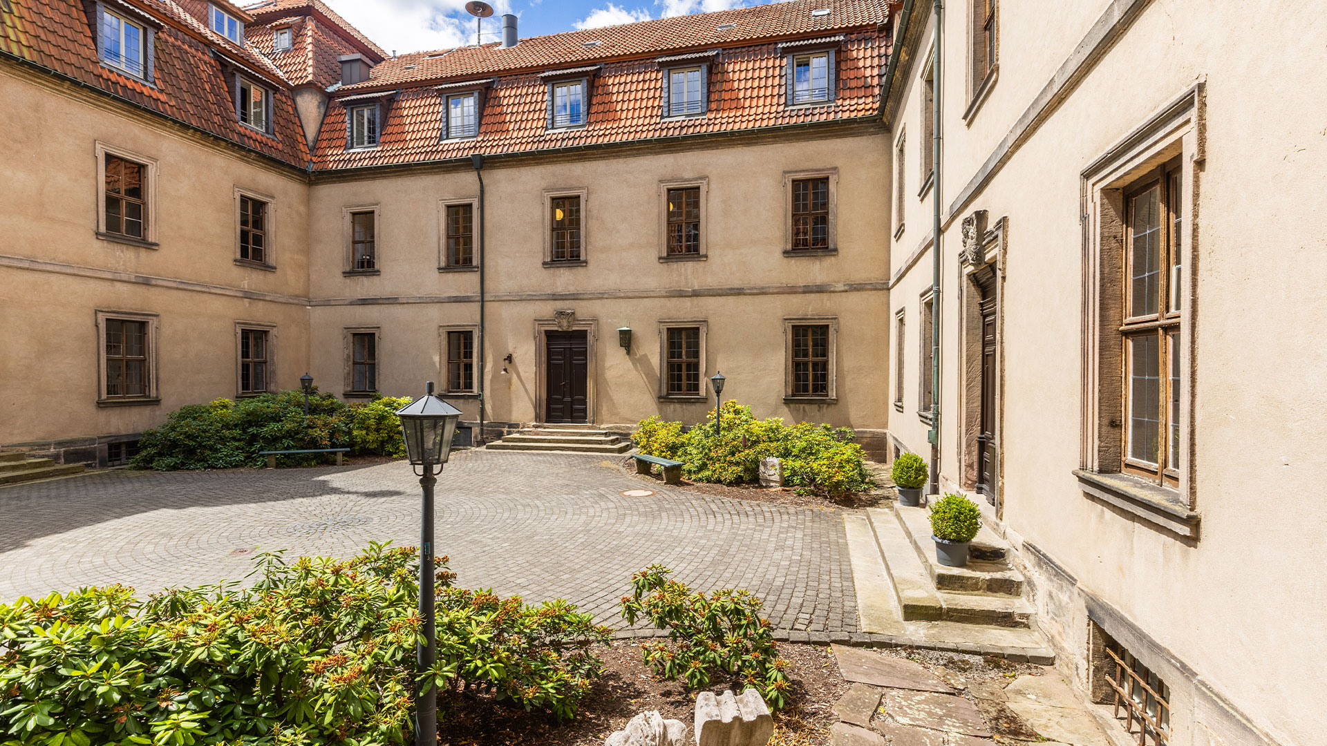 Heller Innenhof mit alten beige Mauern roten Daecher und Blumenbeeten ohne Personen