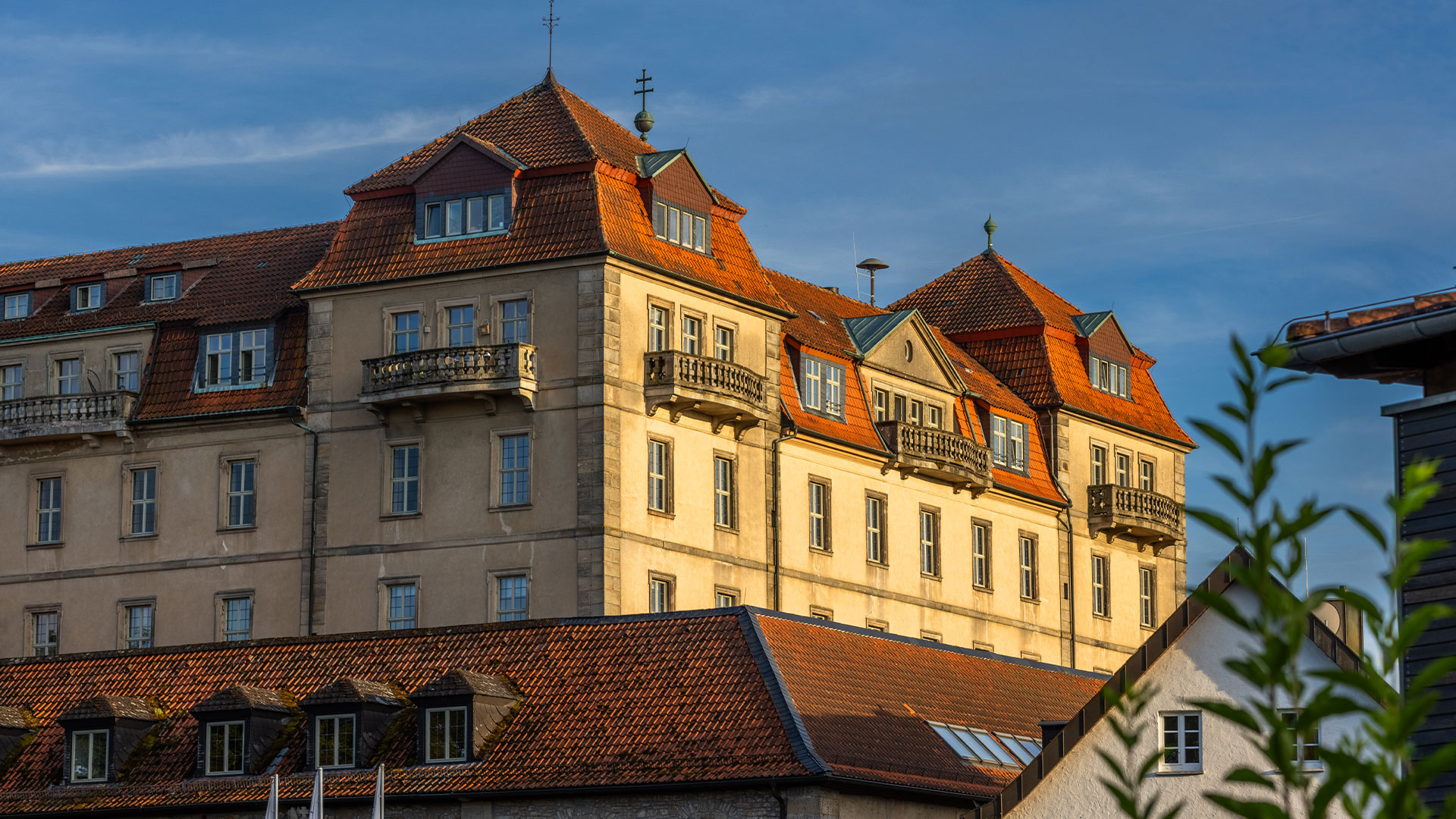 Beiges Haus mit roten Ziegeldaechern im Sonnenlicht und Balkonfenstern