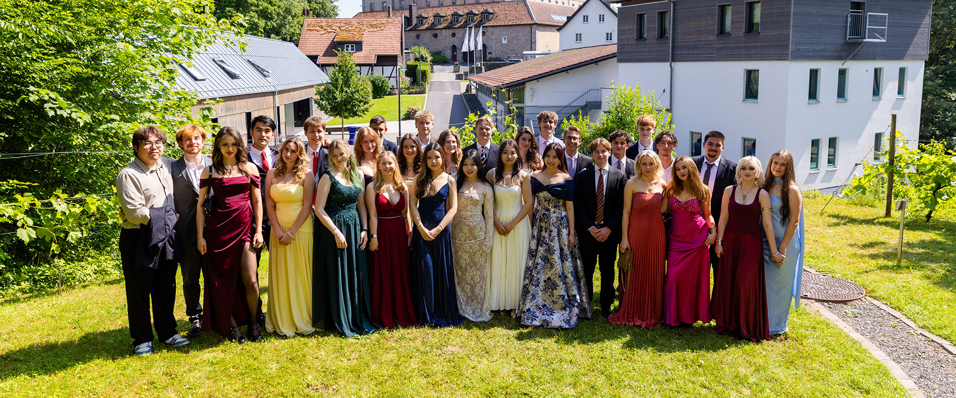 Lachende Gruppe junger Leute in bunten Abendkleidern im Garten bei Sonne