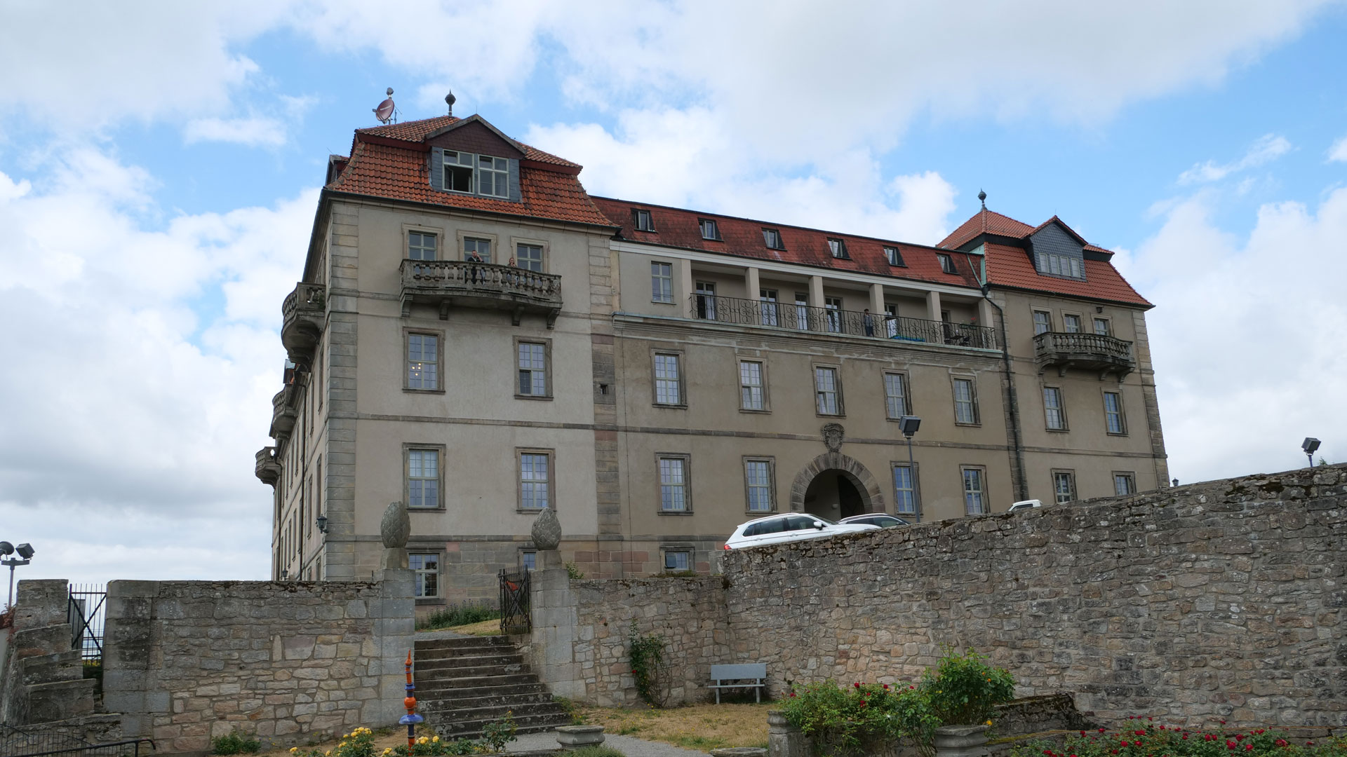 Historisches Schloss mit rotem Ziegeldach hinter alter Steinmauer